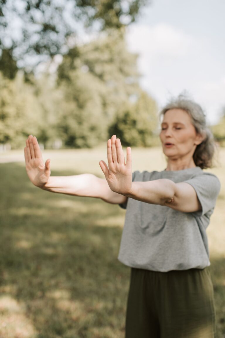 Oudere vrouw doet een rustige qi gong-oefening met gespreide armen en gesloten ogen in een zonnig park